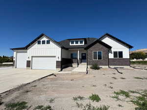 Modern farmhouse style home featuring covered porch, brick siding, driveway, an attached 3rd car garage, and board and batten siding