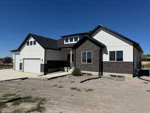 Modern farmhouse with board and batten siding, driveway, an attached 3rd car garage, and brick siding