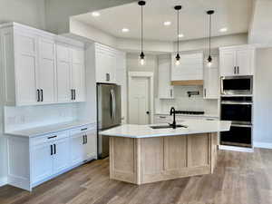 Kitchen with stainless steel appliances, light LVP wood-style floors, tile backsplash, custom white cabinetry, and light quartz countertops