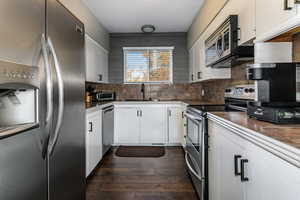 Kitchen with stainless steel appliances, white cabinetry, dark wood-style flooring, decorative backsplash, and dark countertops