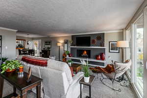 Carpeted living room featuring crown molding, a textured ceiling, and a warm lit fireplace