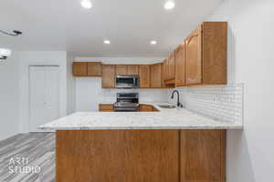 Kitchen featuring light stone countertops, backsplash, stainless steel appliances, recessed lighting, and a peninsula