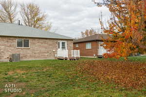 Rear view of property featuring a deck, a shingled roof, a lawn, and brick siding