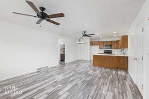 Kitchen with recessed lighting, open floor plan, light countertops, brown cabinetry, and arched walkways