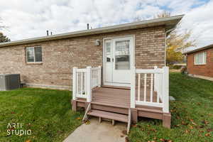 View of exterior entry featuring a yard, a wooden deck, and brick siding