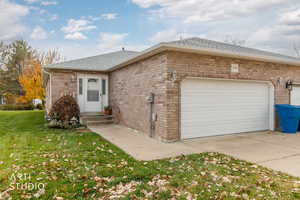 Ranch-style home featuring brick siding, a shingled roof, a front yard, a garage, and driveway