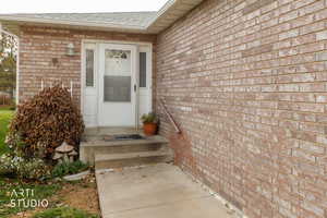 Entrance to property with brick siding and a shingled roof