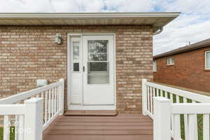 Doorway to property featuring a deck and brick siding