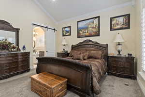 Primary bedroom featuring a barn door, vaulted ceiling, ornamental molding, light colored carpet, and arched walkways