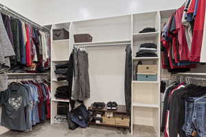 Primary suite spacious walkin closet with light colored carpet