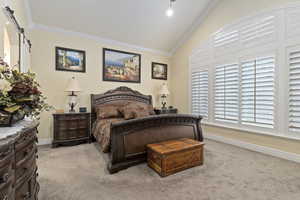 Primary bedroom with vaulted ceiling, crown molding, light colored carpet, and a barn door