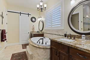Bathroom with two vanities, a bath, a chandelier, and Travertine tile flooring