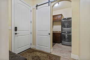 Laundry area featuring cabinet space, a barn door, estacked washer and dryer, and arched walkways