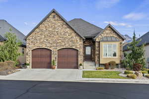 View of front of property with concrete driveway, stucco and stone siding, roof with shingles, and an attached garage