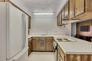 Kitchen with freestanding refrigerator, light countertops, range with electric stovetop, a peninsula, and brown cabinets