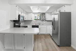 Kitchen featuring appliances with stainless steel finishes, a peninsula, light countertops, light wood finished floors, and white cabinetry