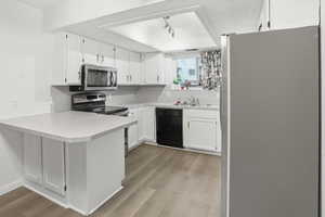 Kitchen with stainless steel appliances, white cabinetry, light countertops, and a peninsula