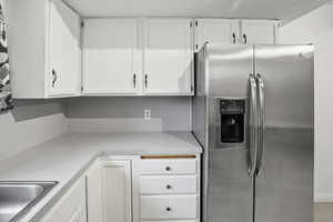 Kitchen with stainless steel fridge, white cabinets, and light countertops