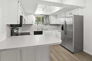 Kitchen with a peninsula, appliances with stainless steel finishes, light countertops, light wood-type flooring, and white cabinets