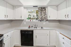 Kitchen with black dishwasher, white cabinets, and light countertops