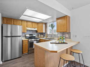 Kitchen featuring stainless steel appliances, light countertops, decorative backsplash, a kitchen bar, and a peninsula