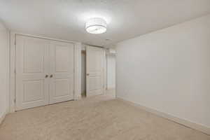 Unfurnished bedroom with a textured ceiling, a closet, and light carpet