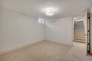 Below grade area featuring a textured ceiling, light colored carpet, and stairway