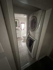 Washroom with stacked washer and clothes dryer and dark tile patterned flooring