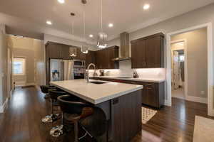 Kitchen with dark brown cabinetry, modern cabinets, a kitchen bar, wall chimney range hood, and appliances with stainless steel finishes