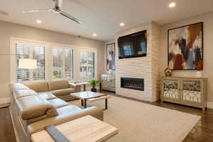Living room with wood finished floors, recessed lighting, a large fireplace, and ceiling fan