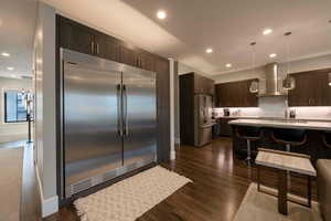 Kitchen featuring a breakfast bar area, dark brown cabinetry, built in fridge, pendant lighting, and recessed lighting