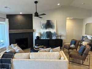 Living area with a large fireplace, lofted ceiling, wood finished floors, a ceiling fan, and recessed lighting