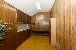 Hallway featuring wooden walls, carpet flooring, vaulted ceiling, and a textured ceiling