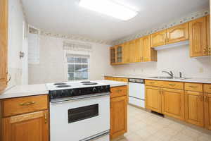 Kitchen featuring white appliances, light countertops, light floors, glass insert cabinets, and brown cabinets