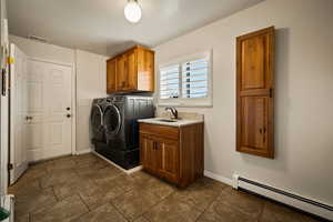 Washroom featuring baseboard heating, independent washer and dryer, cabinet space, a textured ceiling, and dark tile patterned flooring