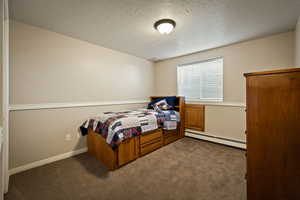 Carpeted bedroom featuring a baseboard heating unit and a textured ceiling