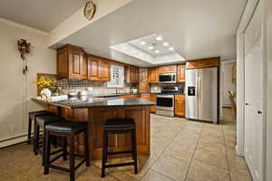 Kitchen with stainless steel appliances, brown cabinets, a peninsula, backsplash, and light tile patterned floors
