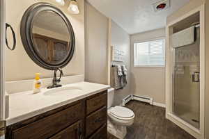 Full bath with vanity, a stall shower, dark wood finished floors, and a baseboard heating unit