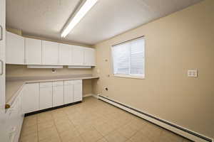 Kitchen featuring a baseboard radiator, light countertops, white cabinetry, a textured ceiling, and light tile patterned floors