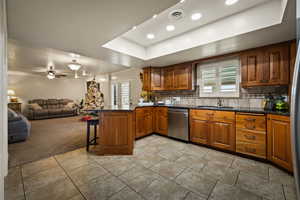 Kitchen featuring brown cabinetry, a breakfast bar area, a raised ceiling, backsplash, and light carpet