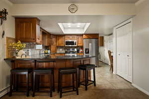 Kitchen with a peninsula, brown cabinetry, stainless steel appliances, light tile patterned floors, and tasteful backsplash