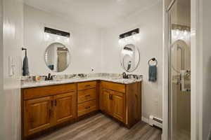 Full bathroom featuring double vanity, a shower stall, dark wood finished floors, and a baseboard heating unit