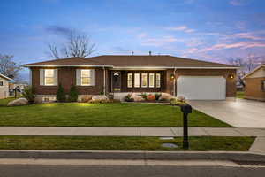 Single story home featuring brick siding, driveway, a yard, an attached garage, and roof with shingles