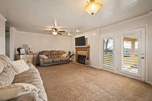 Living area featuring carpet floors, a fireplace, crown molding, a ceiling fan, and a baseboard radiator