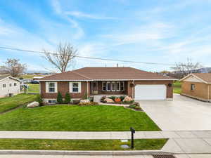 Single story home featuring a porch, driveway, a front yard, and brick siding