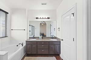 Bathroom featuring a bath, double vanity, plenty of natural light, and dark wood finished floors