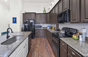 Kitchen featuring black appliances, dark brown cabinets, dark wood-style flooring, decorative backsplash, and dark stone counters