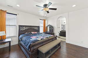 Bedroom with recessed lighting, dark wood-type flooring, ceiling fan, arched walkways, and ensuite bathroom
