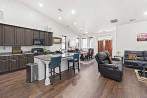 Kitchen with dark brown cabinetry, a kitchen breakfast bar, open floor plan, light stone countertops, and recessed lighting