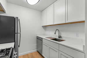 Kitchen with stainless steel appliances, light wood-style flooring, white cabinetry, and light stone counters
